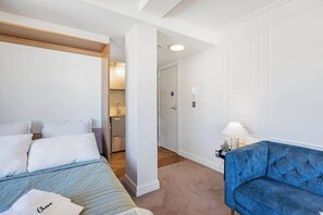 A hotel room with a bed, a blue sofa, a bathroom, and a hallway.