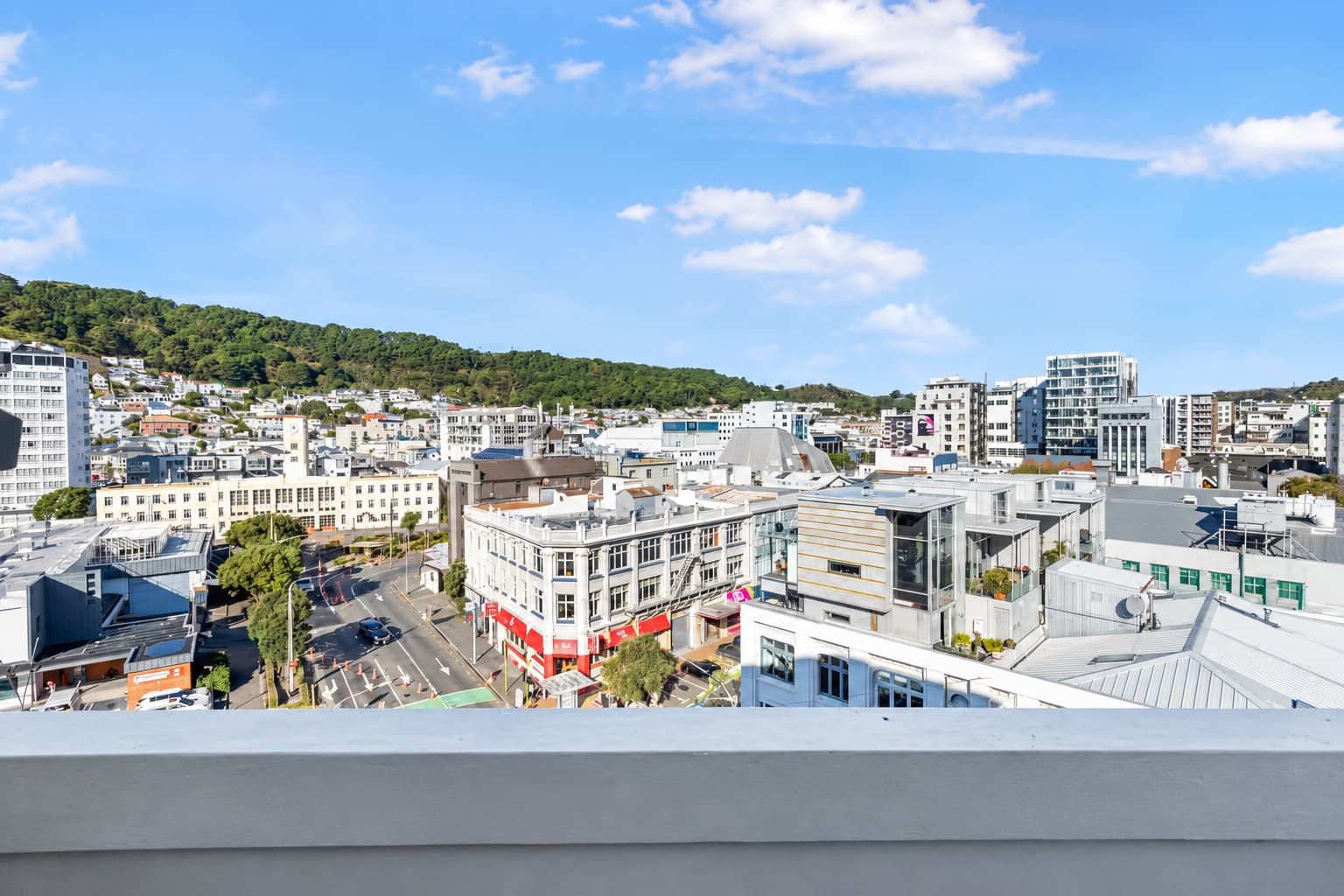A cityscape with modern buildings, a clear sky, and a hilly background.