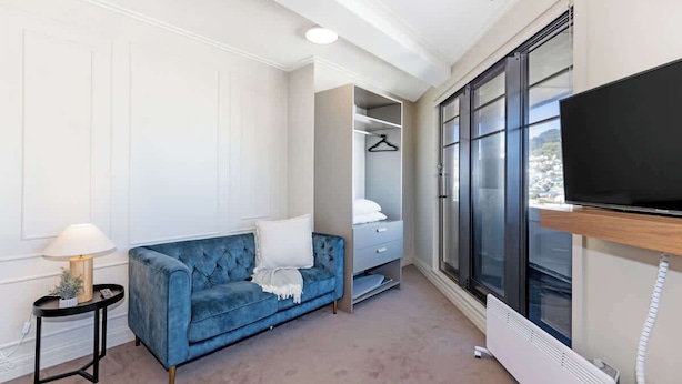 A modern room with a blue sofa, a TV, a heater, and a wardrobe. - 1BR Studio in Te Aro - City Lookout (Wellington)