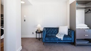 A bedroom with a blue velvet sofa, a bedside table with a lamp, a wardrobe, and a hanging closet. - 1BR Studio in Te Aro - City Lookout (Wellington)