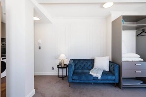 A bedroom with a blue velvet sofa, a bedside table with a lamp, a wardrobe, and a hanging closet.