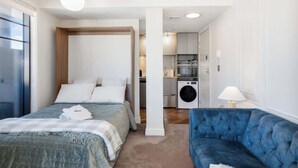 A bedroom with a bed, a blue sofa, a washing machine, and a kitchenette. - 1BR Studio in Te Aro - City Lookout (Wellington)