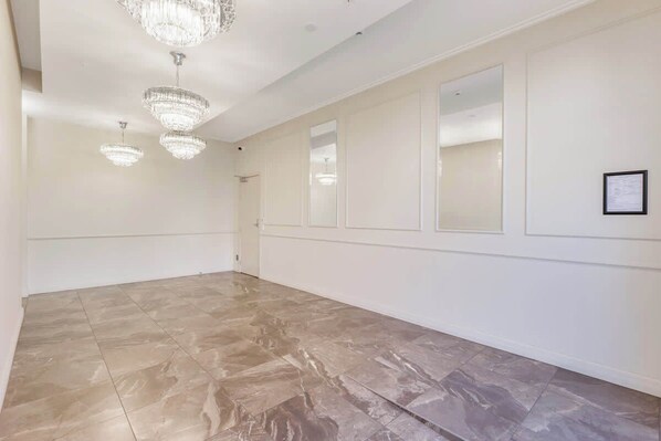 A spacious room with marble flooring, large windows, and three chandeliers.
