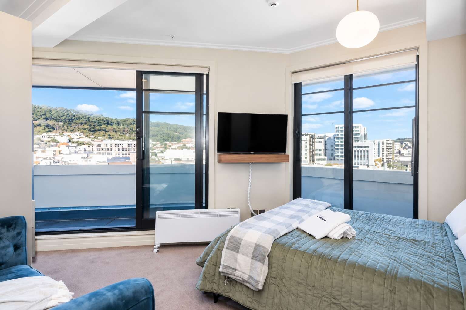 A bedroom with a bed, a television, and a view of a cityscape through large windows.