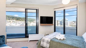 A bedroom with a bed, a television, and a view of a cityscape through large windows.