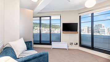 Sala de estar moderna com sofá azul, TV de tela plana na parede e grandes janelas com vista para a cidade.
