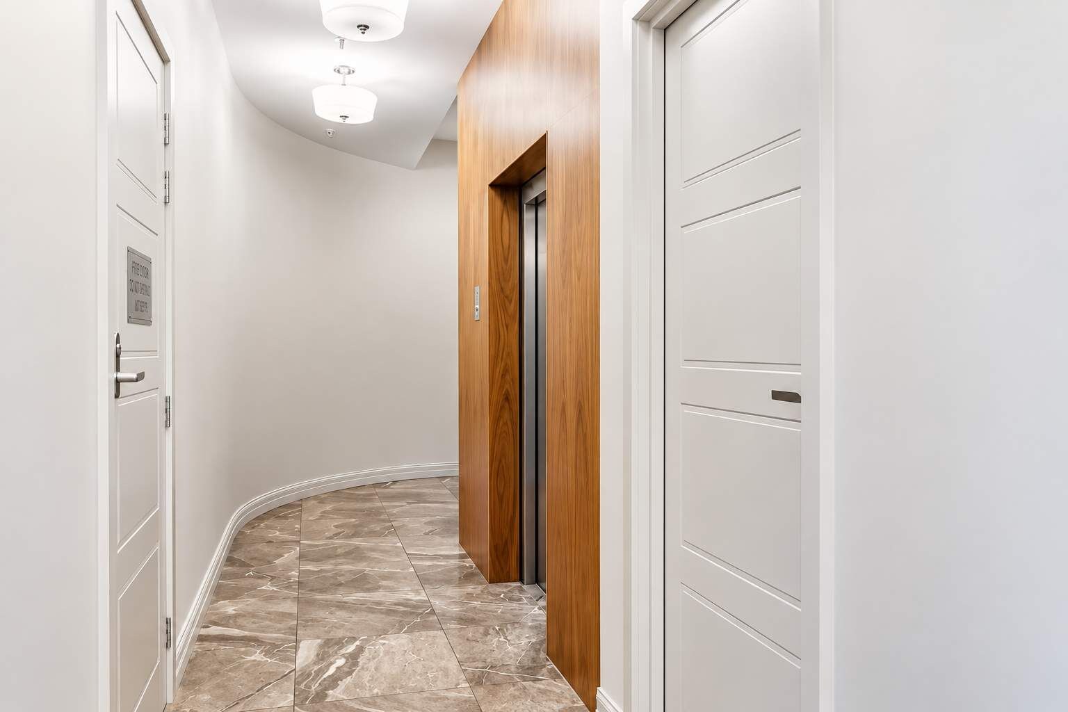 Un pasillo con paredes blancas, una puerta de madera y un suelo de mármol.