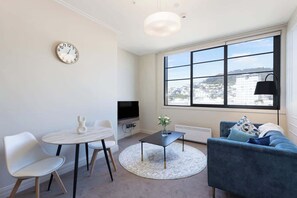 A modern living room with a round table, two chairs, a sofa, a TV, and a large window with a city view.