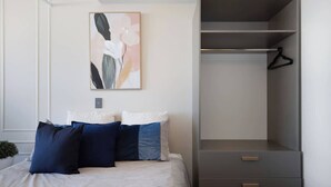 A bedroom with a bed, a grey wardrobe, and a framed abstract painting on the wall. - Cityview Studio + Kitchen | Wellington CBD (Wellington)
