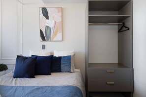 A bedroom with a bed, a grey wardrobe, and a framed abstract painting on the wall.