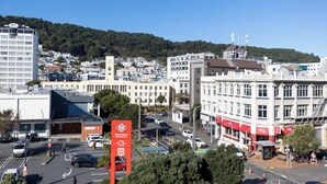 Stadsgezicht met een opvallend hotel met een rood-witte gevel, een parkeerplaats en een heuvel op de achtergrond.