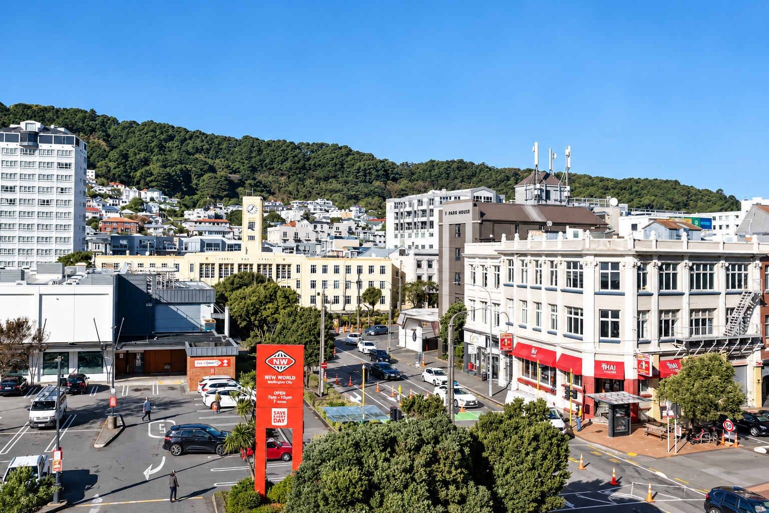 A cityscape with a prominent red sign, a variety of buildings, and a hilly background.