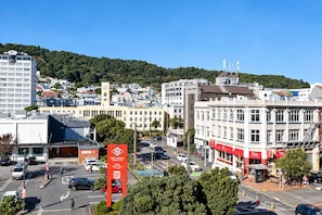 A cityscape with a prominent red sign, a variety of buildings, and a hilly background. - Cityview Studio + Kitchen | Wellington CBD (Wellington)