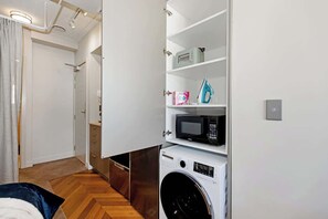 A compact laundry room with a washing machine, a microwave, and storage shelves.