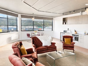 A modern living room with leather sofas, a glass coffee table, and a view of a cityscape through large windows.