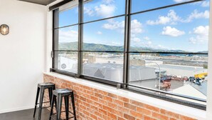 A room with a large window, brick wall, two black stools, and a view of an airport.