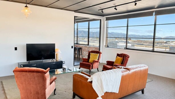 A modern living room with a TV, leather sofas, and large windows offering a view of the landscape.
