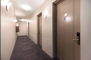 A hotel hallway with a carpeted floor, light fixtures on the walls, and a door with a keypad lock. - Mt Victoria Studio - Kitchen, Bath Tub, Sleeps 2 (Wellington)