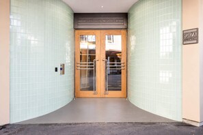 A building entrance with a tiled wall, a double door with a glass panel, and a sign indicating 'CRANMEIR SQUARE.' - Mt. Victoria Studio | Bath + Full Kitchen (Wellington)