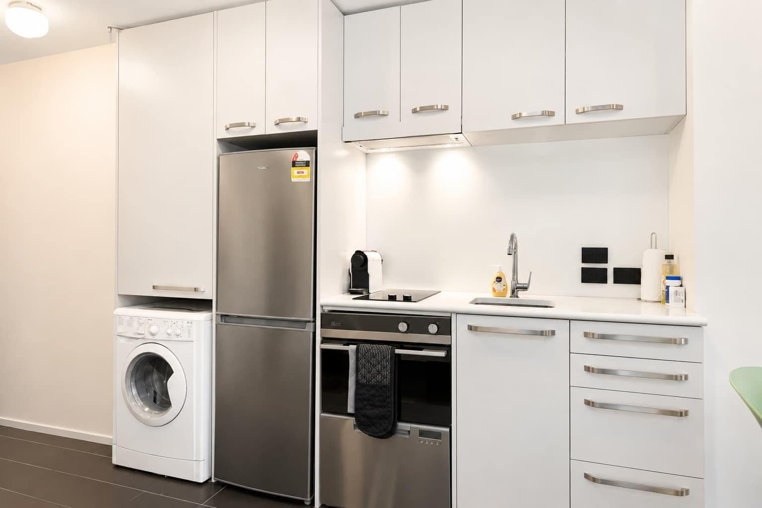 A modern kitchen with stainless steel appliances, a built-in washing machine, and a compact layout.