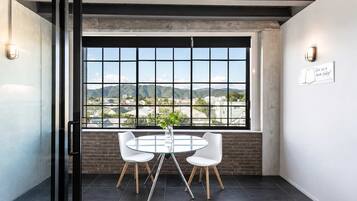 A modern conference room with a large window, two white chairs, a glass table, and a brick wall.