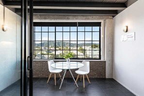 Une salle de conférence moderne dotée d’une grande fenêtre, de deux chaises blanches, d’une table en verre et d’un mur en briques.