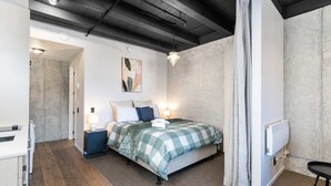 A modern bedroom with a bed, bedside lamps, a radiator, and a view of a hallway. - Petone Studio Stay | Balcony + Bath and Tub (Lower Hutt)