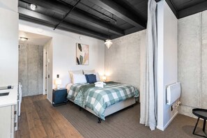 A modern bedroom with a bed, bedside lamps, a radiator, and a view of a hallway. - Petone Studio Stay | Balcony + Bath and Tub (Lower Hutt)