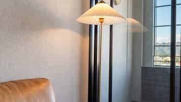 A leather sofa in a corner with a floor lamp and a view through a glass door to an interior space.
