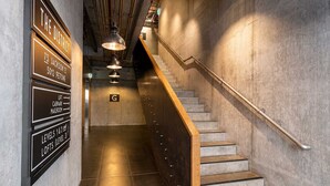 A staircase with a wooden handrail and metal balusters, leading to a landing with a sign indicating 'The District' and directions to 'LIFT, CARPARK, MAILROOM'. - Petone Studio Stay | Balcony + Bath and Tub (Lower Hutt)