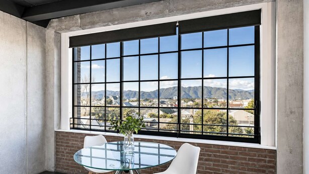 A room with a large window, a glass table, two white chairs, and a potted plant. - Petone Studio Stay | Balcony + Bath and Tub (Lower Hutt)