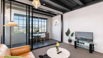 Uma sala de estar moderna com sofá de couro, mesa de centro redonda, televisão e uma janela ampla com vista para o exterior.