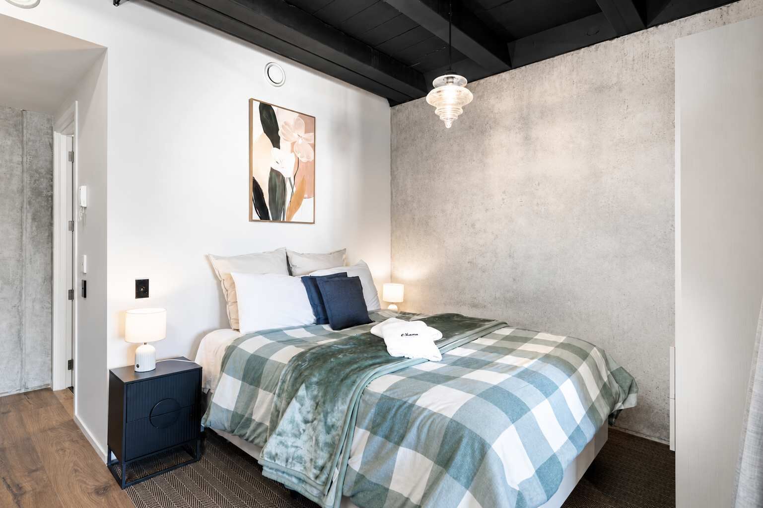 Quarto com uma cama, duas mesas de cabeceira, luminária pendente e uma obra de arte na parede.