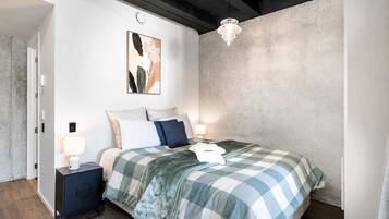 Quarto com uma cama, duas mesas de cabeceira, luminária pendente e uma obra de arte na parede.