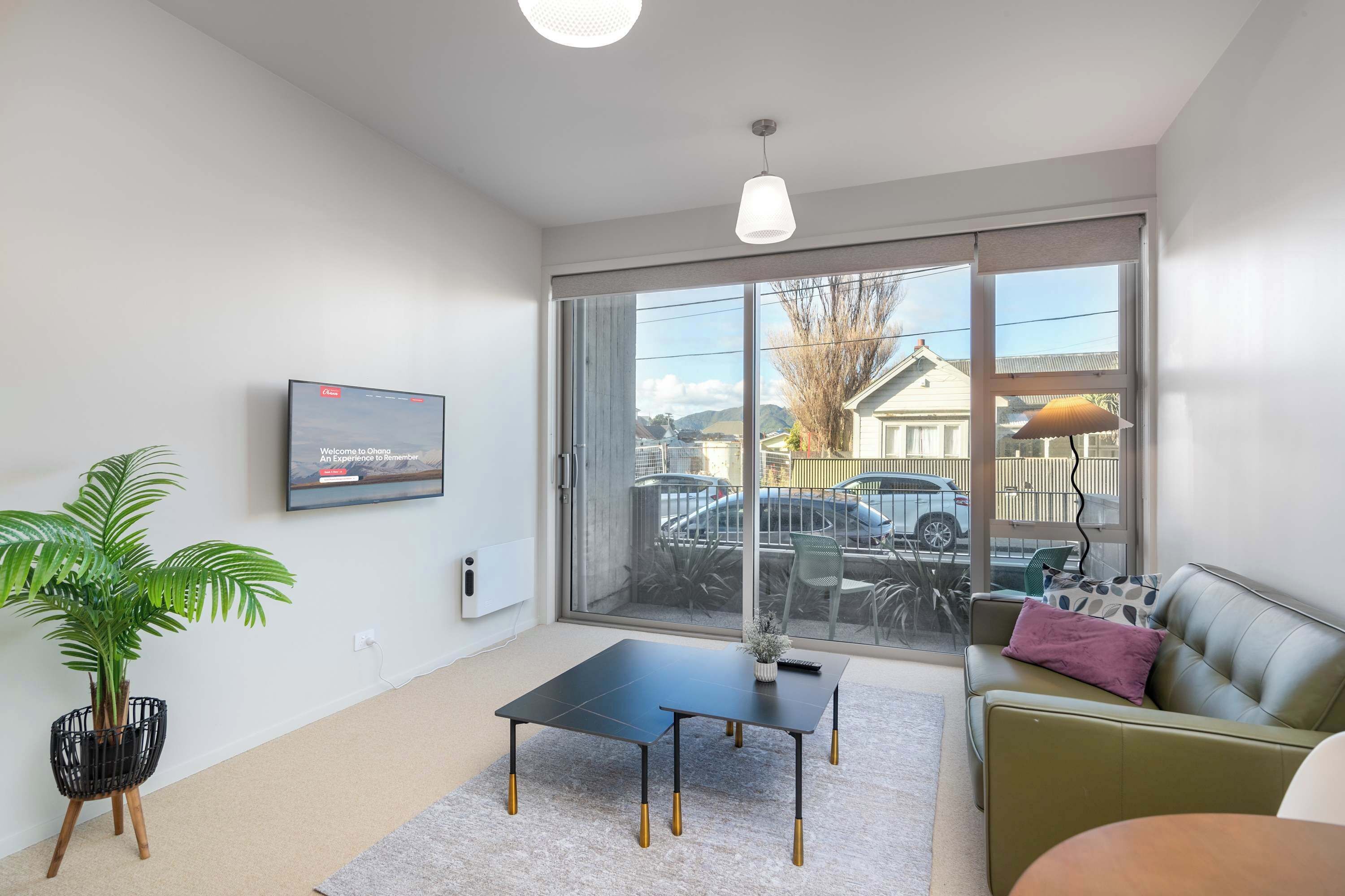 Un salon moderne avec un canapé, une table basse, une plante en pot et un téléviseur fixé au mur.