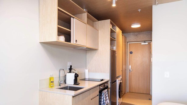 A compact kitchenette with a sink, a coffee maker, a toaster, and a small oven. There is a door leading to a bedroom. - Petone Studio - Balcony, Bath Tub, Sleeps 2 (Lower Hutt)