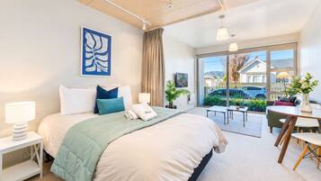 A modern hotel room with a large bed, a desk, and a balcony with a view.