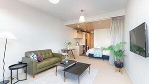 A modern hotel room with a sofa, a coffee table, a TV, a dining area, and a bed. - Petone Studio - Balcony, Bath Tub, Sleeps 2 (Lower Hutt)