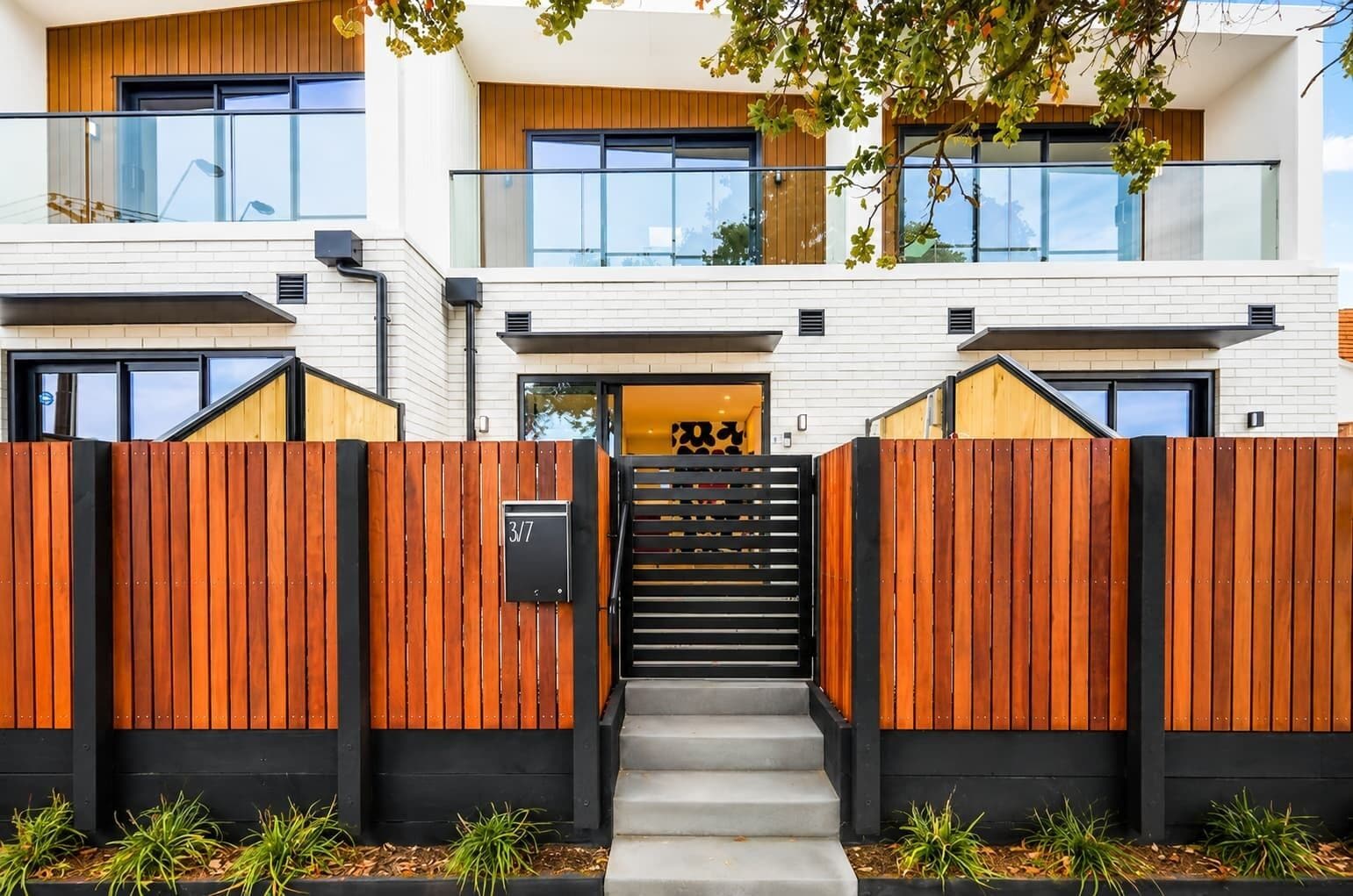 A modern two-story building with a wooden fence, a staircase leading to the entrance, and a sign indicating the address.