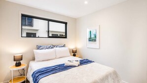 Habitación de hotel con cama, dos mesitas de noche, ventana y un cuadro enmarcado en la pared.