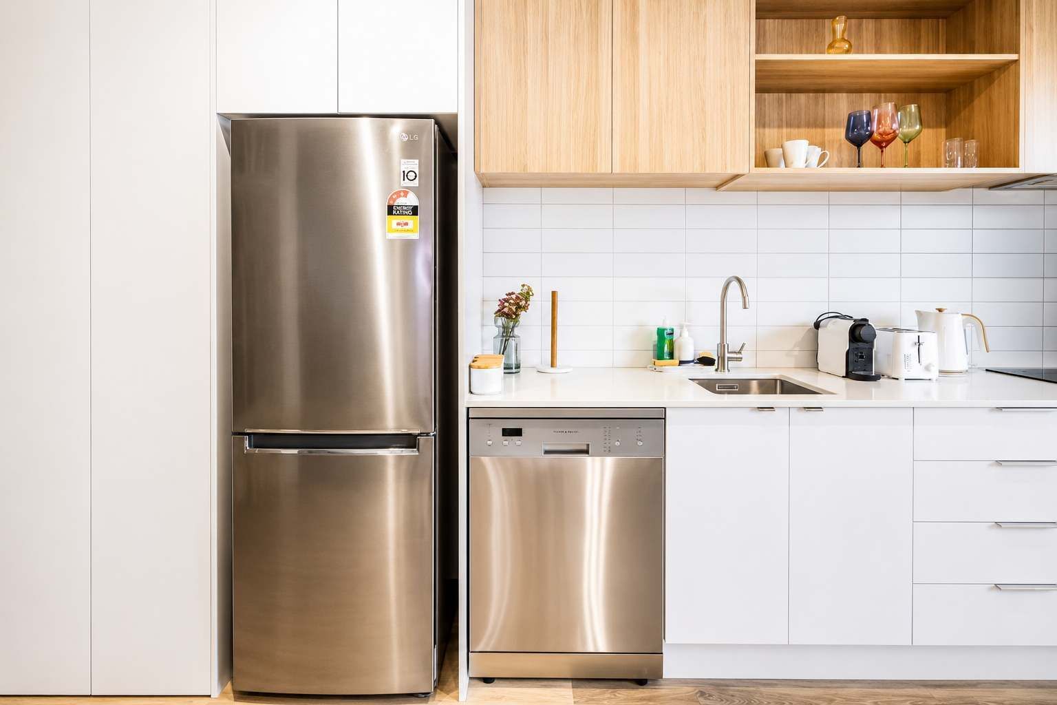 Cocina moderna con electrodomésticos de acero inoxidable, incluyendo un refrigerador y lavavajillas, armarios blancos y una encimera de madera.