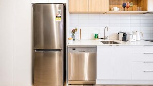 Cocina moderna con electrodomésticos de acero inoxidable, incluyendo un refrigerador y lavavajillas, armarios blancos y una encimera de madera.