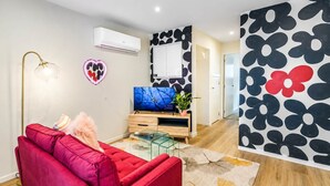 Una sala de estar moderna con un sofá rojo, una mesa de centro de vidrio, un televisor de pantalla plana y un aire acondicionado instalado en la pared.