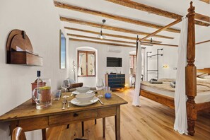A room with a wooden table set for dining, a bed with a canopy, and a television on the wall. - Bella Ciao Studio (Rovinj)