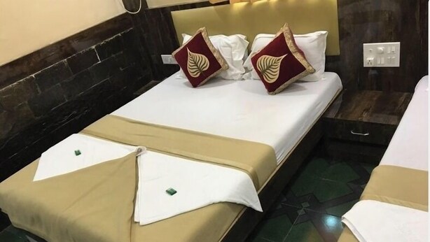 Una cama bien tendida con ropa de cama blanca y beige, dos almohadas decorativas y una mesita de noche con una lámpara.