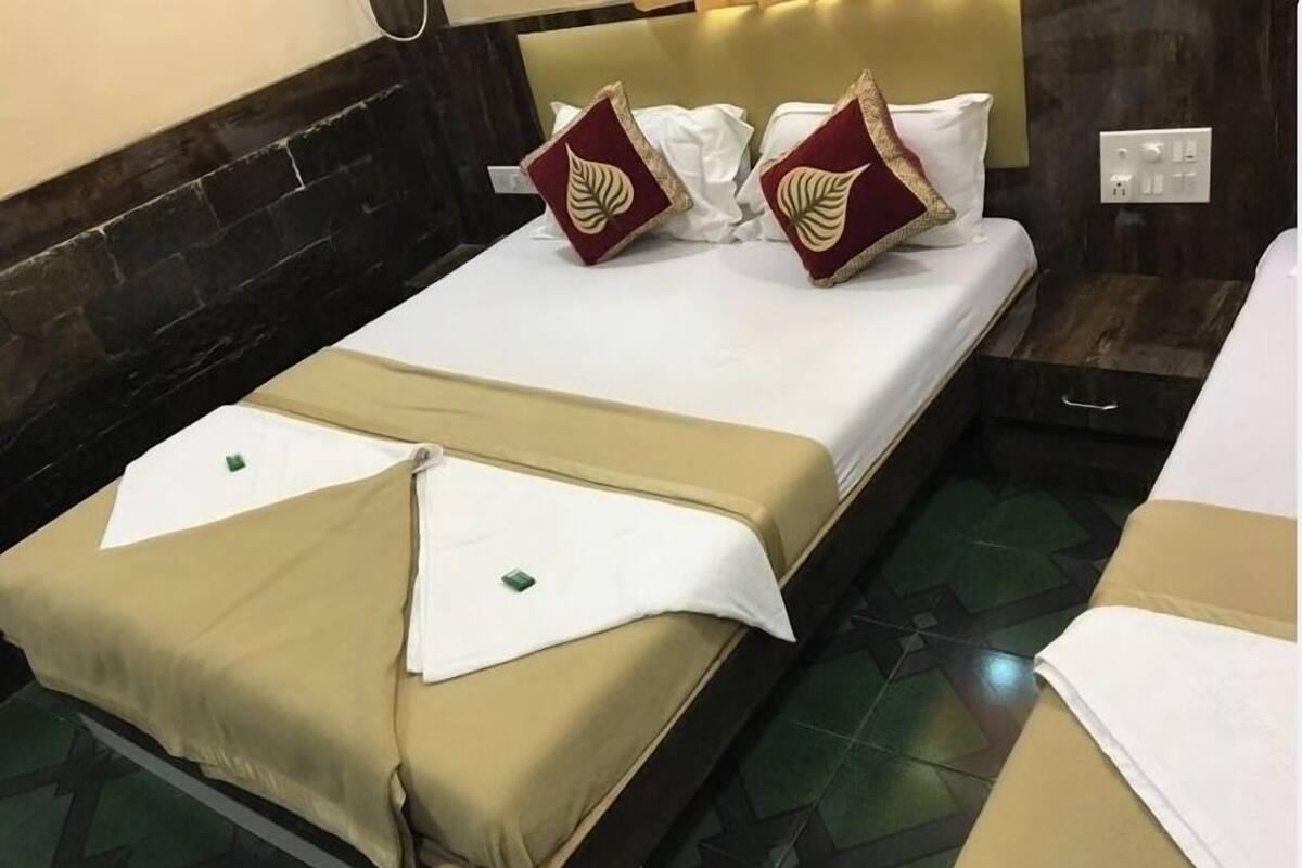 Una cama bien tendida con ropa de cama blanca y beige, dos almohadas decorativas y una mesita de noche con una lámpara.