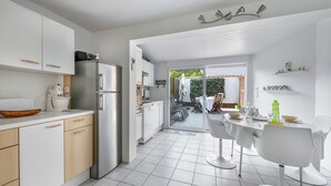 A modern kitchen with white cabinets, a stainless steel refrigerator, and a dining area with a white table and chairs. - Sea view, beach 50m away, House for 4, terrace (La Plaine-sur-Mer)