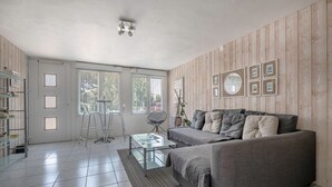 A modern living room with a grey sofa, a glass coffee table, and a wooden wall. - Sea view, beach 50m away, House for 4, terrace (La Plaine-sur-Mer)