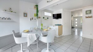 A modern dining area with a white table set for four, white chairs, and a kitchen in the background. - Sea view, beach 50m away, House for 4, terrace (La Plaine-sur-Mer)
