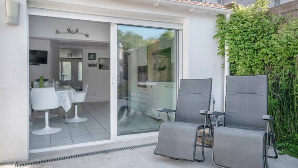 A patio with two grey chairs, a table, and a sliding glass door leading to an indoor dining area. - Sea view, beach 50m away, House for 4, terrace (La Plaine-sur-Mer)